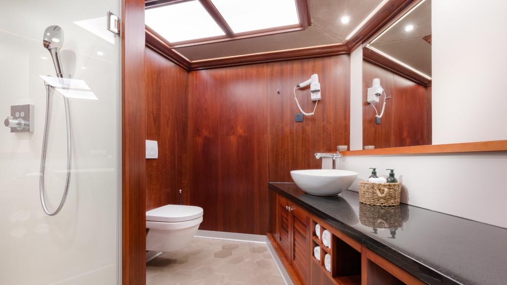 Ein aus edlem Holz verkleidetes Bad mit Dusche, Toilette, Waschbecken und Einbauschränken.